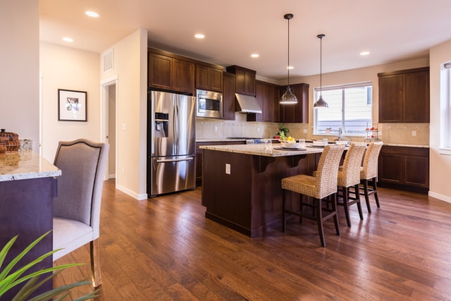 a kitchen with dark brown cabinets and a stainless steel fridge that has a large centre island lined with fabric covered chairs